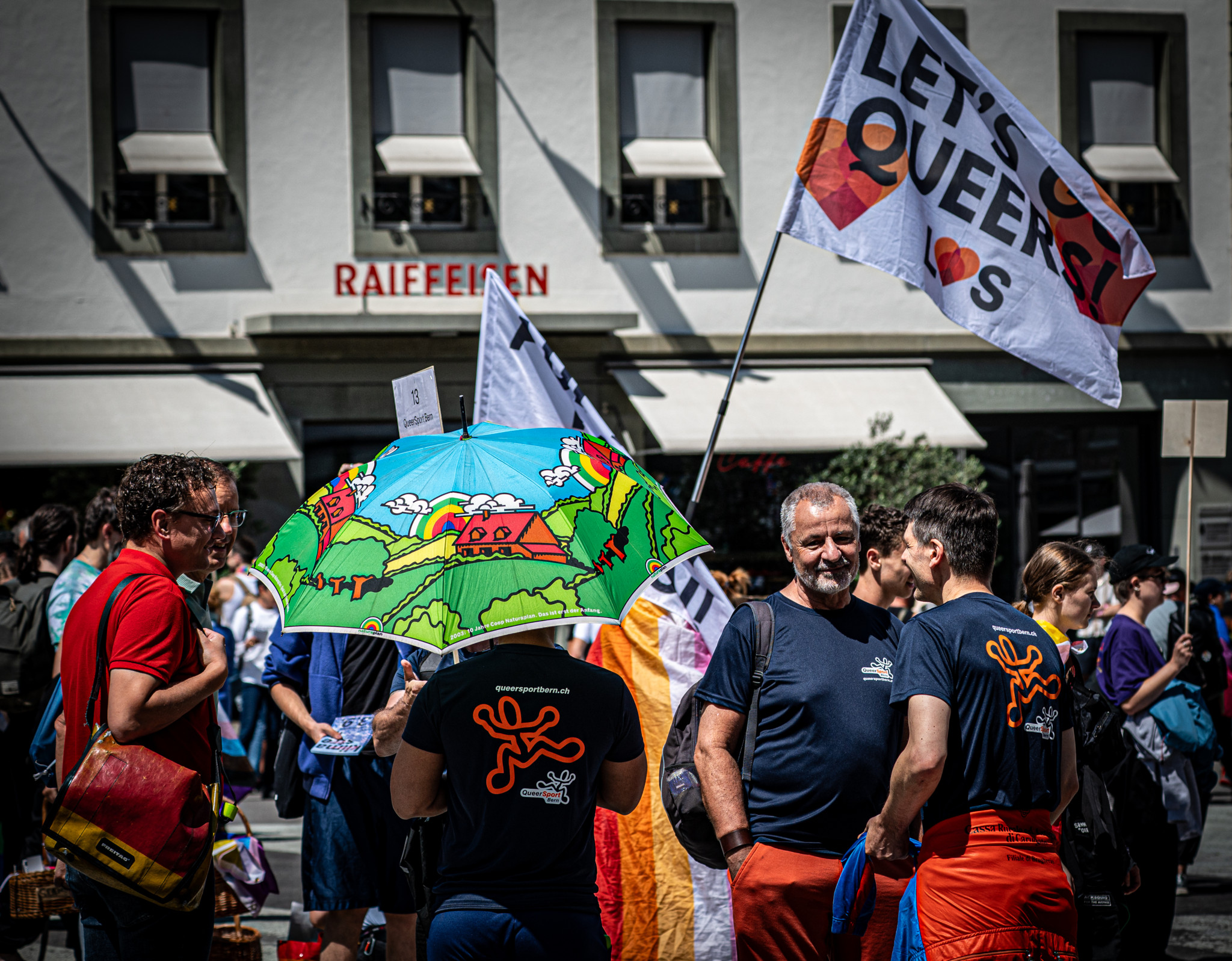 Menschen bei einer LGBTQ±Demonstration mit Regenbogenfarben und ’Let’s Queer It!’ Flagge in einer städtischen Umgebung. Menschen bei einer LGBTQ±Demonstration mit Regenbogenfarben und ’Let’s Queer It!’ Flagge in einer städtischen Umgebung.