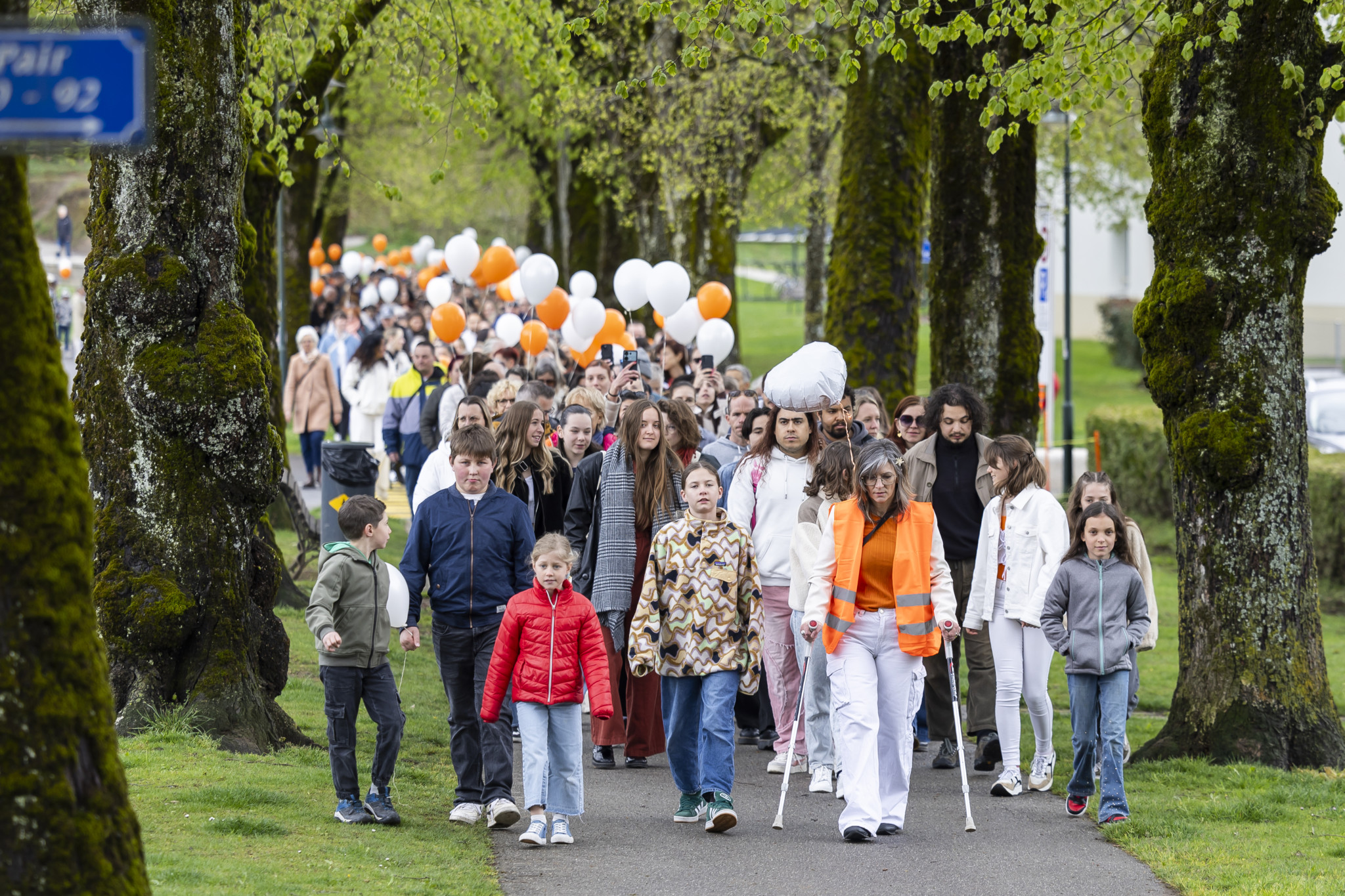Des participants à une marche blanche à Bulle, tenant des ballons blancs et orange, en hommage à une victime de féminicide. Des participants à une marche blanche à Bulle, tenant des ballons blancs et orange, en hommage à une victime de féminicide.
