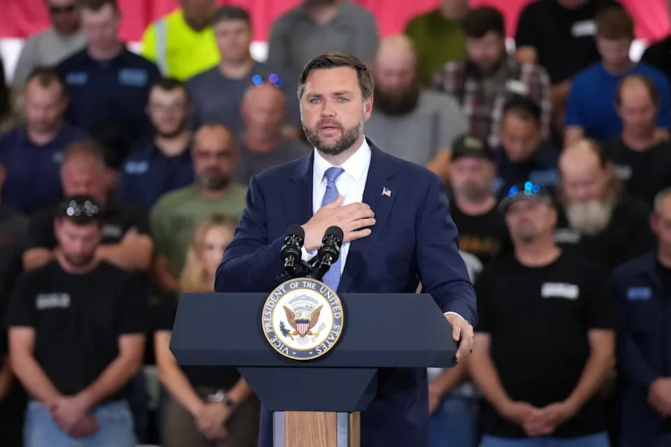 A person in a suit speaks at a podium with a Vice Presidential seal, in front of a crowd wearing casual attire