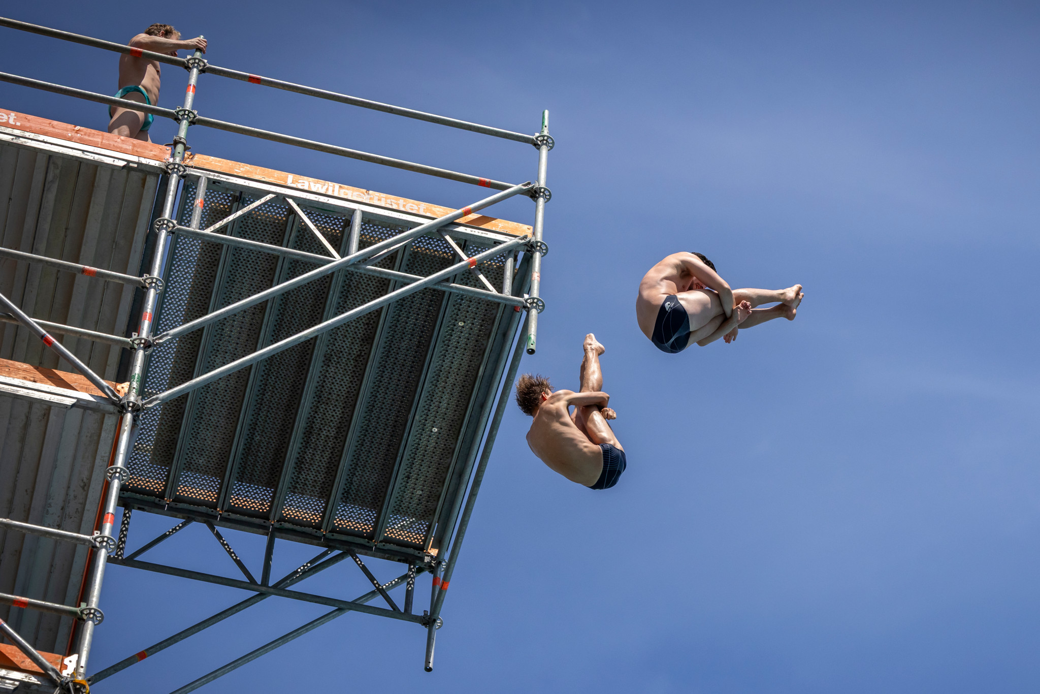 Deux plongeurs effectuent des figures aériennes lors du Lancy Cliff Diving à la piscine de Marignac à Genève.