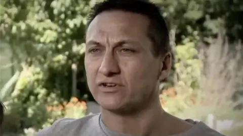 Nine/A Current Affair Dezi Freeman is photographed. He has dark hair and stands in front of a garden.