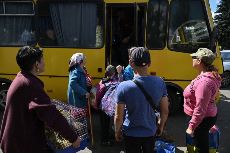 people carrying their belongings get onto a yellow bus