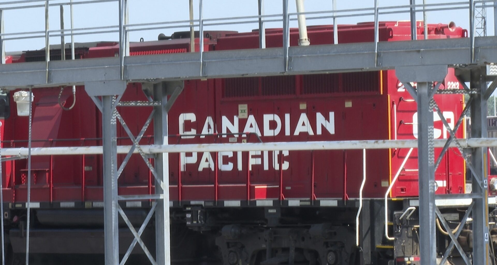 A red Canadian Pacific locomotive is partially obscured by metal railings and structures in an industrial setting.