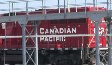 A red Canadian Pacific locomotive is partially obscured by metal railings and structures in an industrial setting.