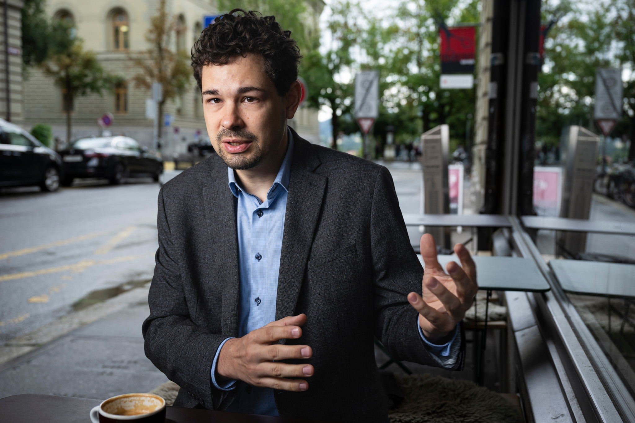 Samuel Kullmann spricht in einem Strassencafé in Bern, während er eine Tasse Kaffee auf dem Tisch vor sich hat.