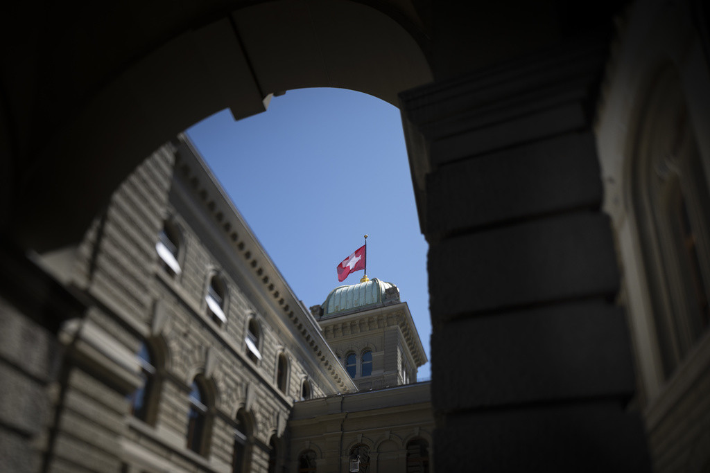 Schweizer Fahne weht auf der Kuppel des Bundeshauses, aufgenommen durch den Durchgang zum Besuchereingang in Bern.