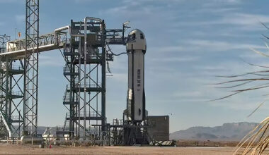 a white rocket topped by a gumdrop-shape capsule sits on its launch pad in a mountain valley.