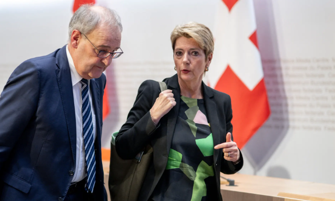 Karin Keller-Sutter et Guy Parmelin discutent devant des drapeaux suisses. Karin Keller-Sutter et Guy Parmelin discutent devant des drapeaux suisses.