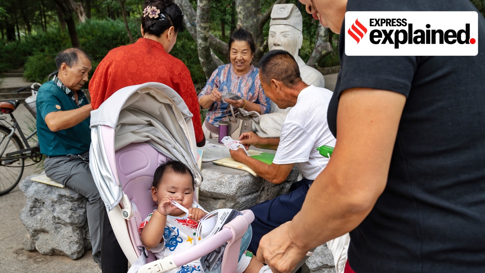 China fertility subsidy: A group of older residents plays cards near a baby in a stroller at a park in Miyun, a district in Beijing, Sept. 18, 2024.