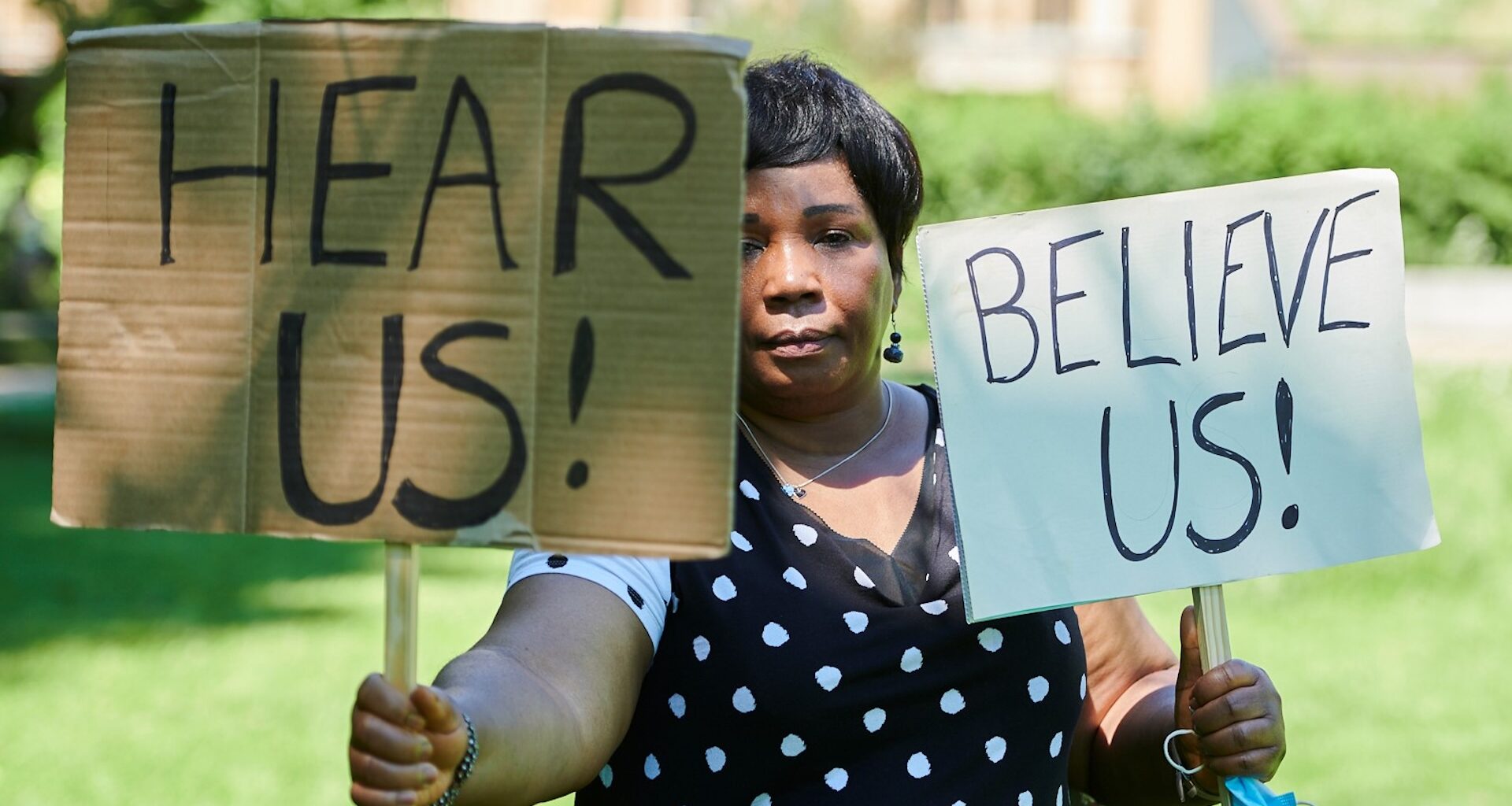 A woman holding a sign calling for people to 'Hear us' and 'Believe us'. Image: Simon Tang/ Women for Refugee Women