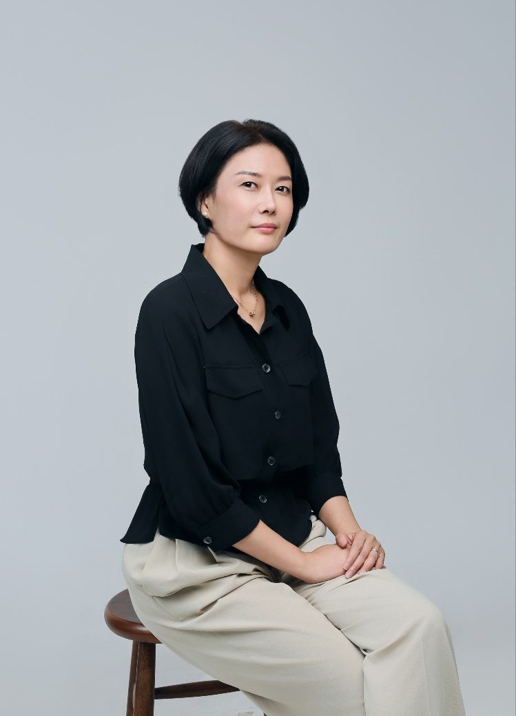Eunice Jung seated for a portrait in a black shirt and beige trousers.