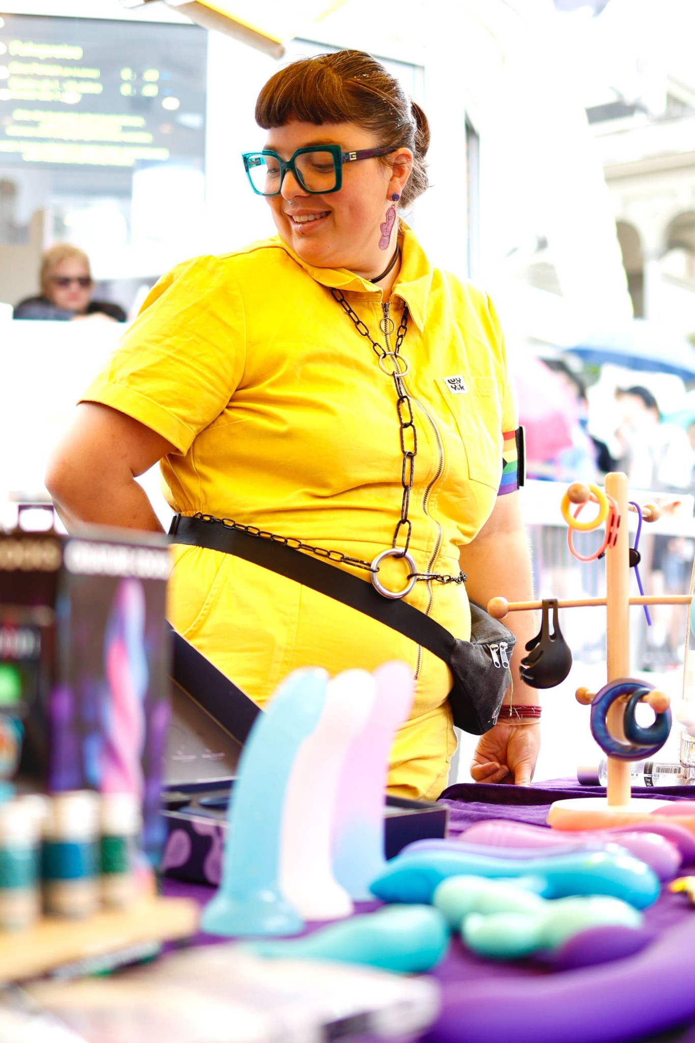 Frau in gelbem Outfit steht an einem Marktstand, der bunte Produkte verkauft, darunter Spielzeuge und Flaschen. Frau in gelbem Outfit steht an einem Marktstand, der bunte Produkte verkauft, darunter Spielzeuge und Flaschen.