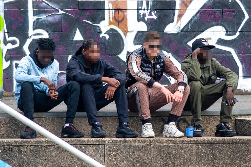 Four young men sitting on a wall against a graffitied background.