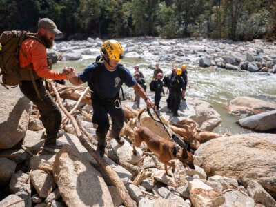 A civilian search and rescue team member, left, gives a hand to a member of a FEMA urban search and rescue team as they hike along the Broad River in the aftermath of Hurricane Helene on October 2, 2024 near Chimney Rock, North Carolina.