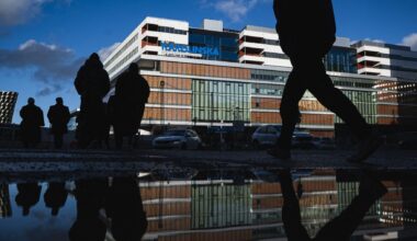 Building of Karolinska University Hospital in Stockholm reflecting in wet pavement, outline of people walking