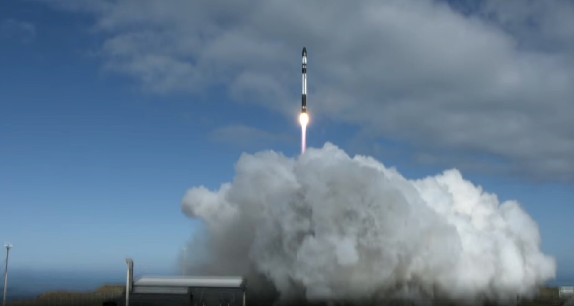 a black and white rocket launches into a cloudy sky, generating a large plume of grayish exhaust