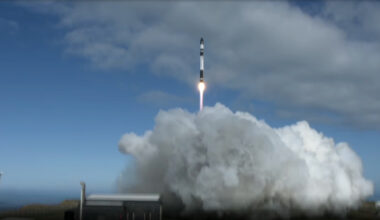 a black and white rocket launches into a cloudy sky, generating a large plume of grayish exhaust
