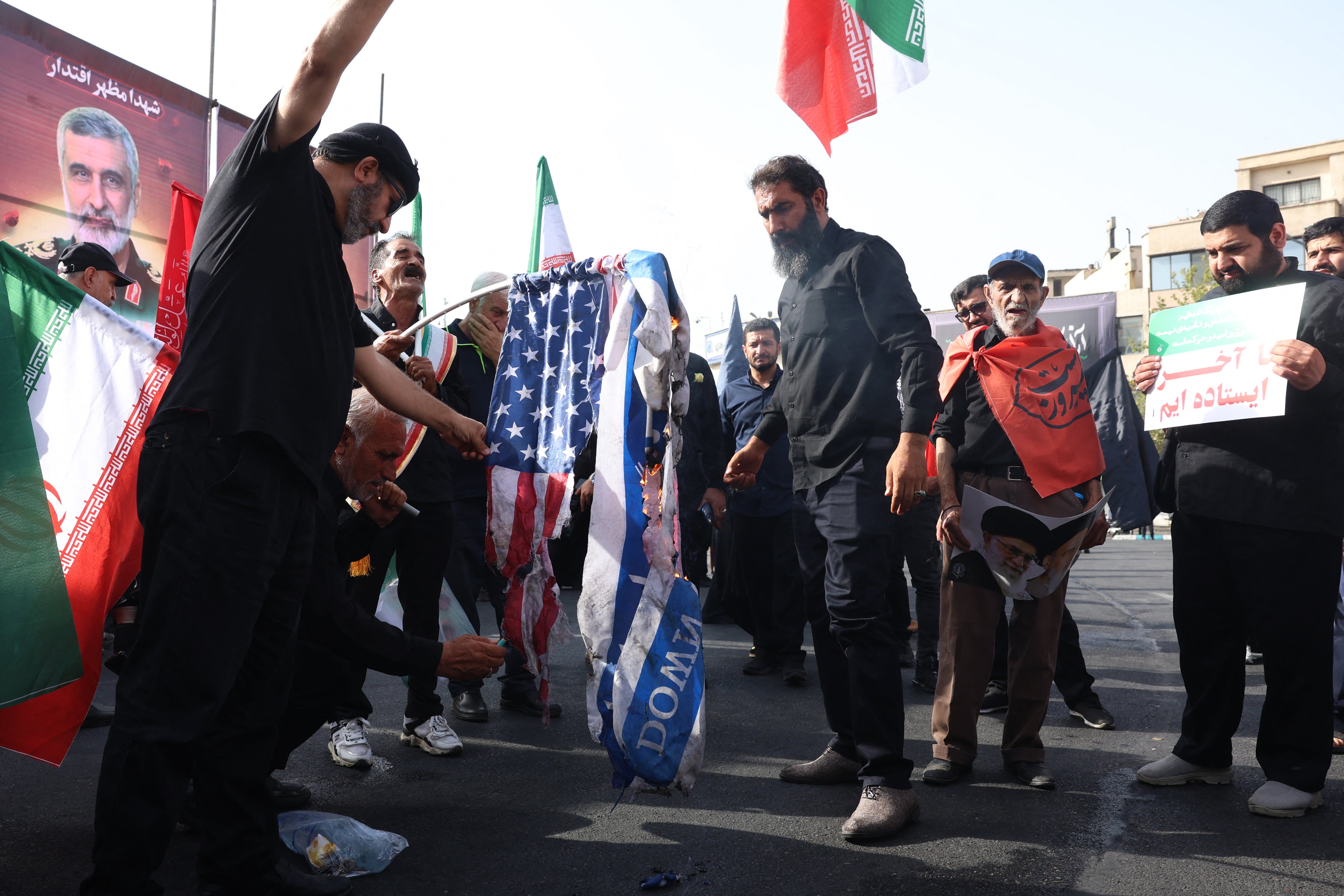Iranians burn the US and Israeli flags during a funeral ceremony for Iranian IRGC generals and scientists who were killed in recent Israeli airstrikes, in Tehran, on June 28, 2025.