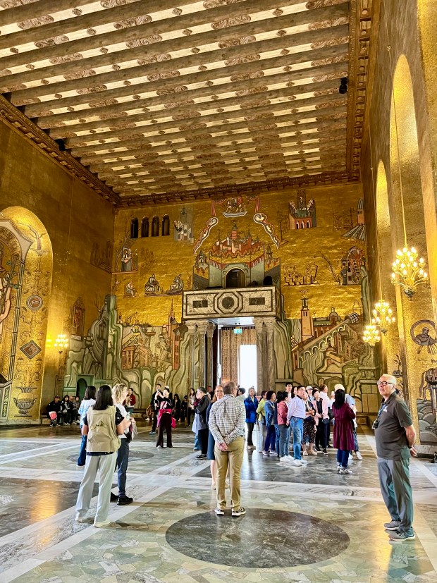 A room covered in gold-leaf mosaics is full of people