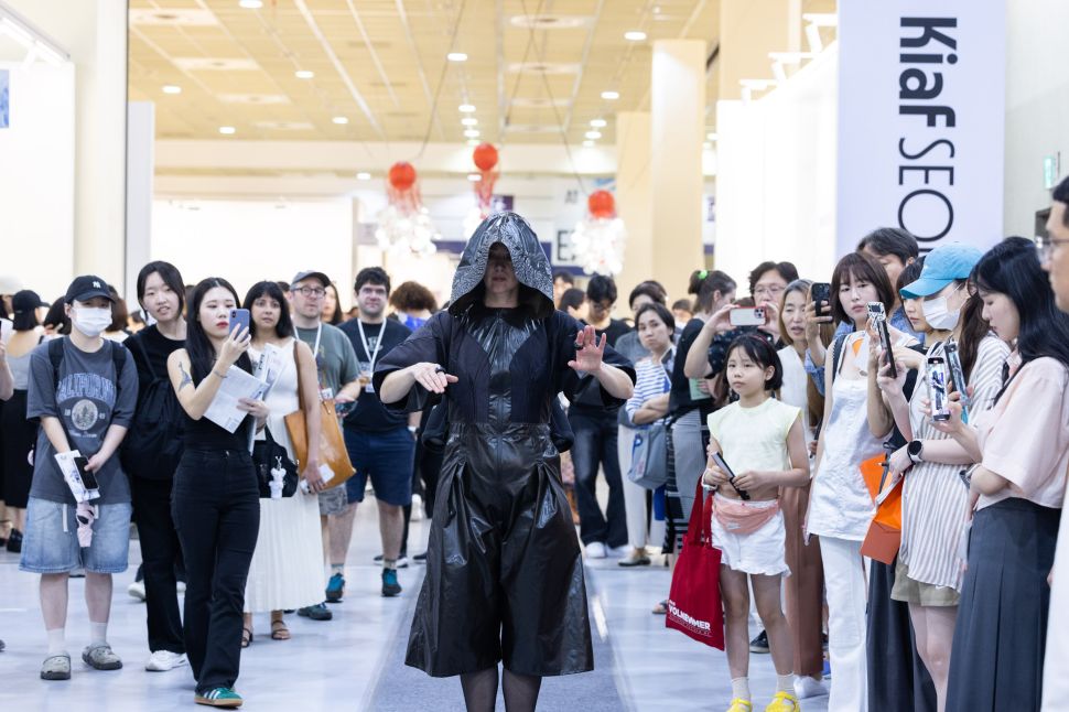 Performer in hooded costume walks through audience at Kiaf SEOUL.