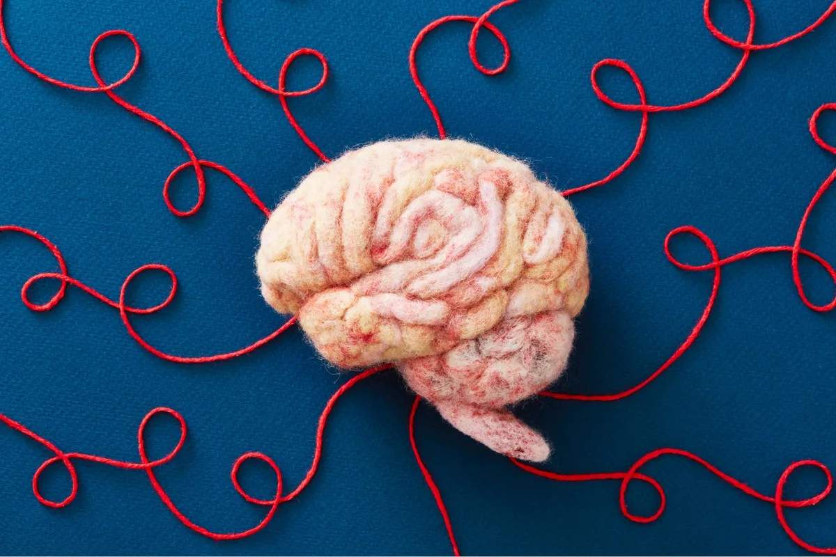 A model of a brain made out of wool, on a blue background, with red strings spiralling outwards.