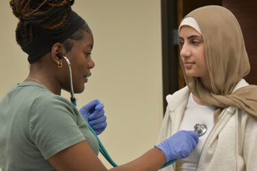 Imani Smith (left), a rising ninth grader at Sylvan Hills Junior High School in Sherwood, uses a stethoscope to check another student’s heart rate during an activity that demonstrated how health professionals rely on data to inform their decisions in patient care.