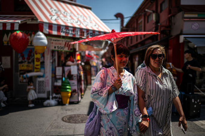 Tourists share a traditional umbrella to shelter from the sun while walking along a shopping street at the Asakusa district near Sensoji Temple, on a hot day in Tokyo on July 28, 2025. Photo by AFP
