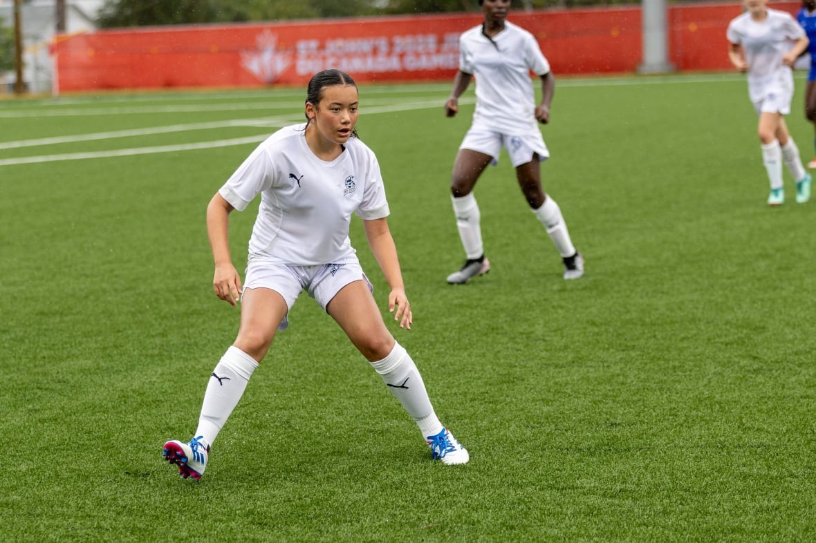 A young female soccer player dressed in white gear.