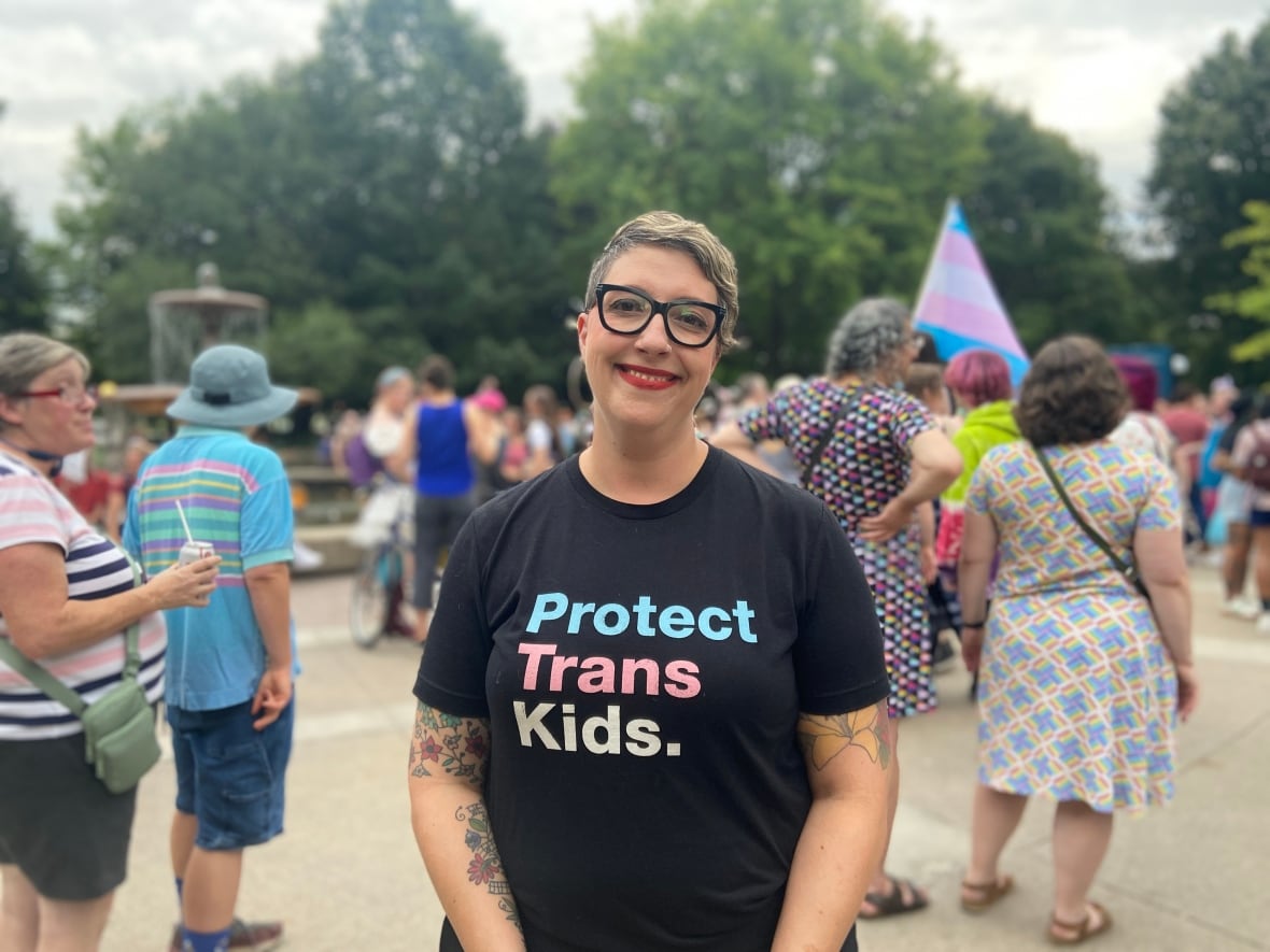 Ottawa City Councillor Ariel Troster poses for a photo in Confederation Park wearing a black t-shirt that reads "Protect Trans Kids" 