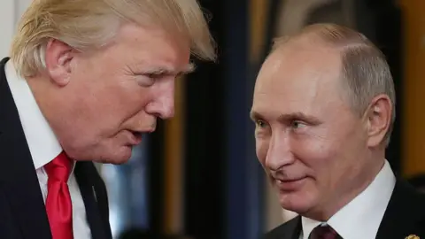 Getty Images A close of up Putin looking left at Trump as he speaks to him at the Asia-Pacific Economic Cooperation (APEC) leaders' summit in 2017. Trump is wearing a red tie, and both leaders are pictured in front of a blurred background. 