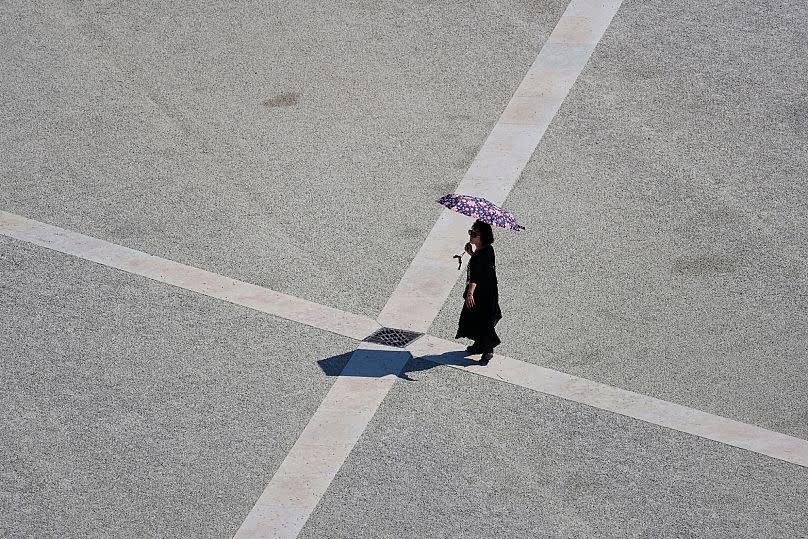 Une femme utilise un parapluie pour se protéger du soleil alors qu'elle traverse la place du Comercio à Lisbonne par une chaude journée, samedi 2 août 2025.