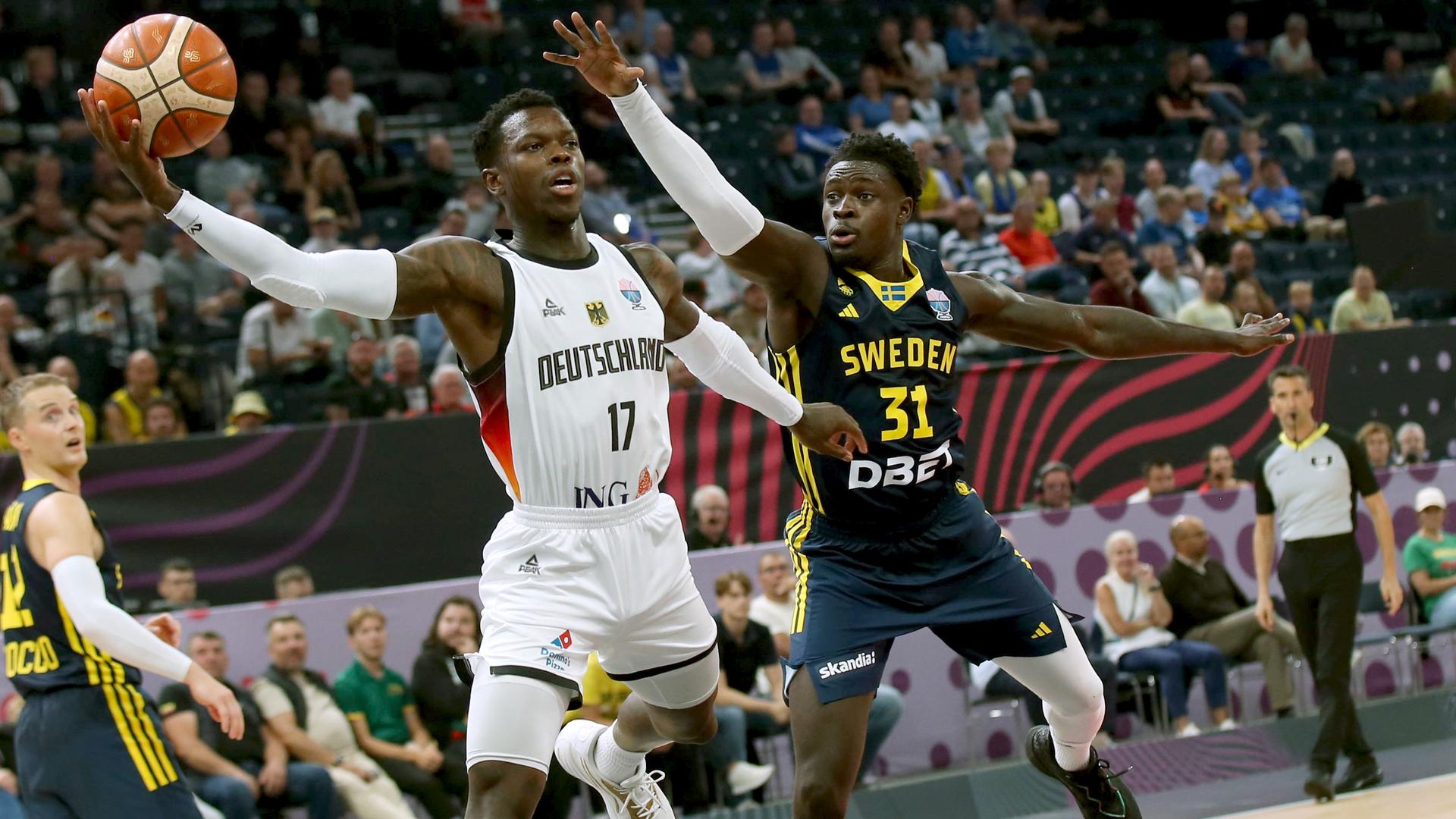 Das Bild zeigt Baskeballer Dennis Schröder beim Korbwurf, neben ihm ist ein Gegenspieler zu sehen.