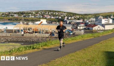 A man running along a path with green grass either side. He is wearing all black.