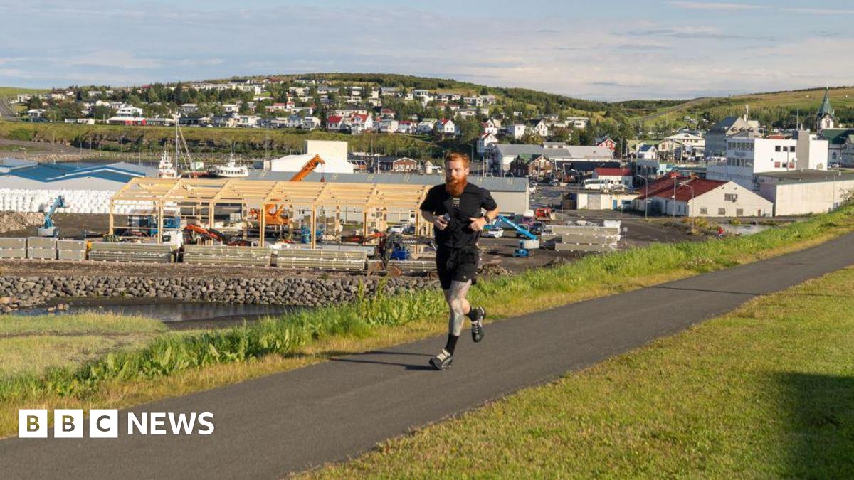 A man running along a path with green grass either side. He is wearing all black.