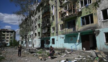 Eine Frau läuft über eine mit Trümmern übersäte Straße. Vor einem zerstörten Gebäude sitzt ein Mann.