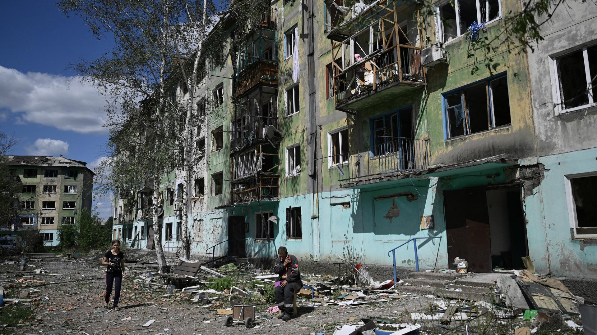 Eine Frau läuft über eine mit Trümmern übersäte Straße. Vor einem zerstörten Gebäude sitzt ein Mann. Eine Frau läuft über eine mit Trümmern übersäte Straße. Vor einem zerstörten Gebäude sitzt ein Mann.