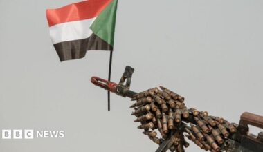 A Sudanese flag placed above the muzzle of a machine gun covered with an ammunition belt.