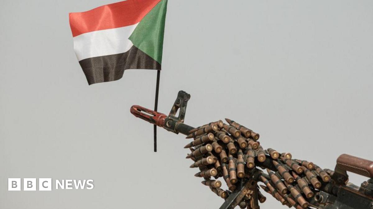 A Sudanese flag placed above the muzzle of a machine gun covered with an ammunition belt.