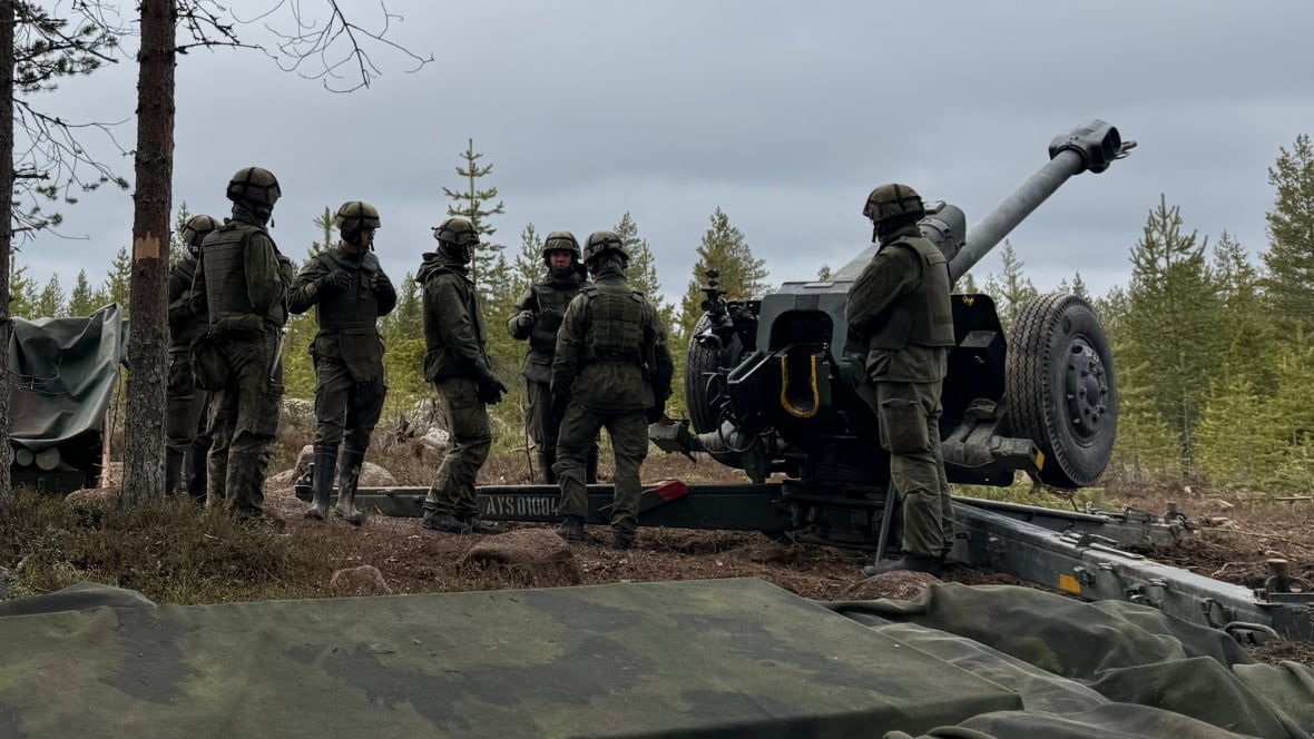 Men in military uniforms stand next to a large cannon.