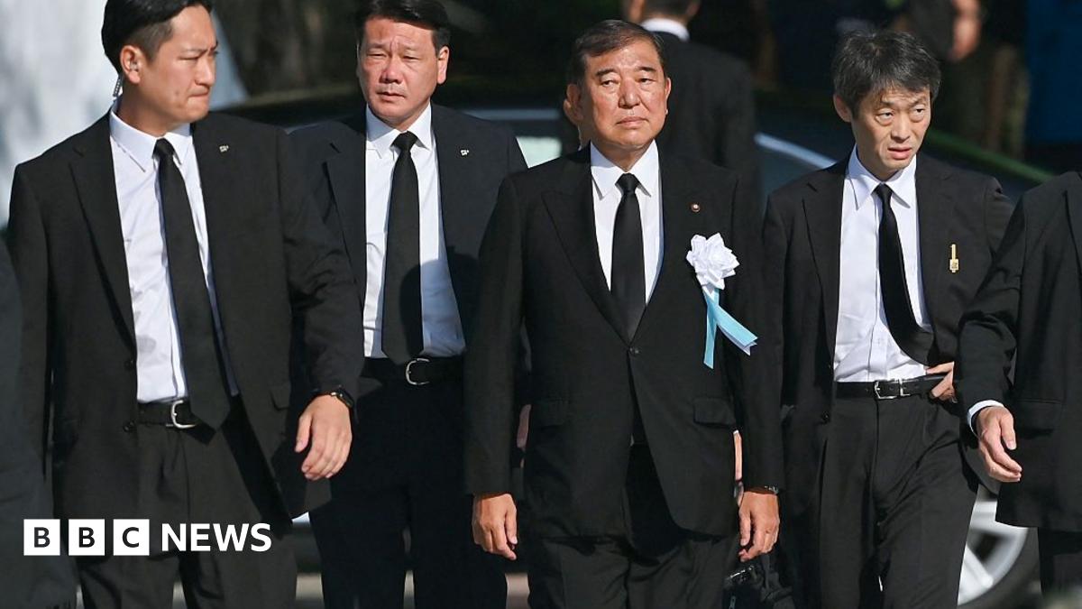 Ishiba wearing a black suit walking. He is flanked by other men in black suits.