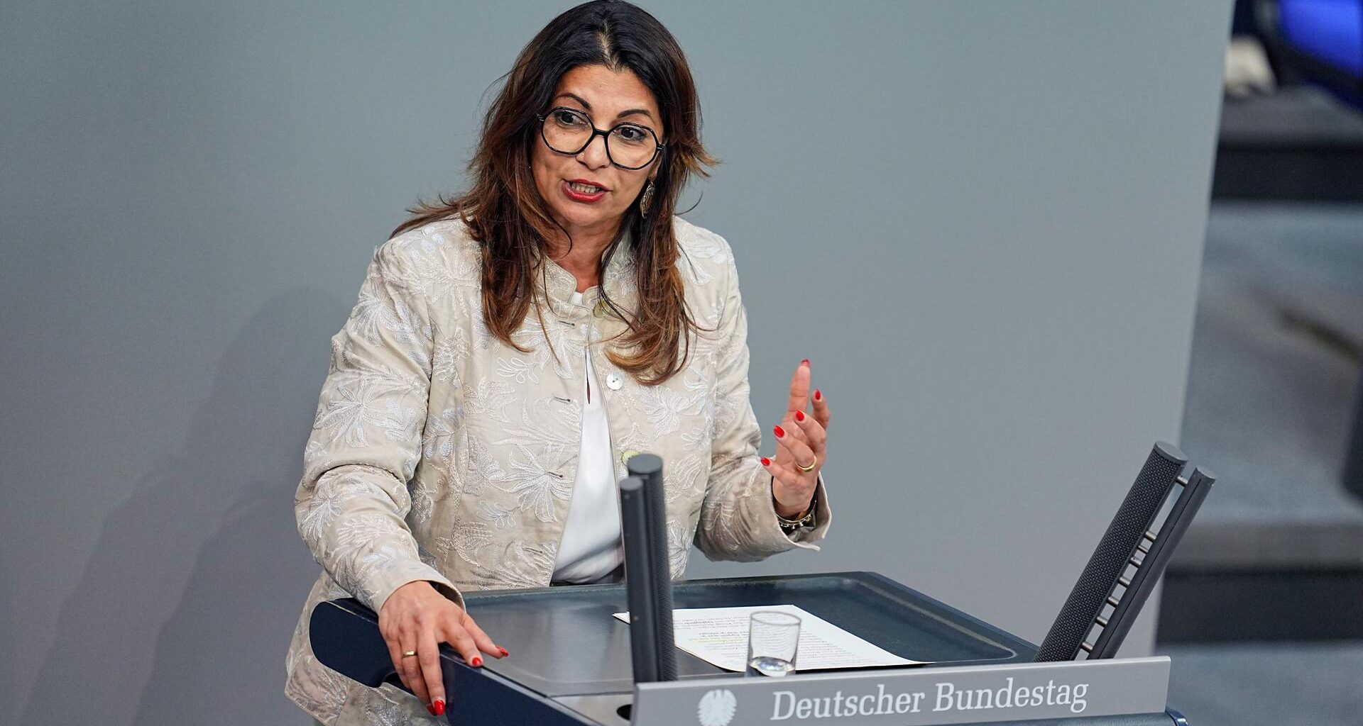 Die dunkelharige Politikerin steht im beigefarbenen Jackett am Rednerpult und sagt etwas.