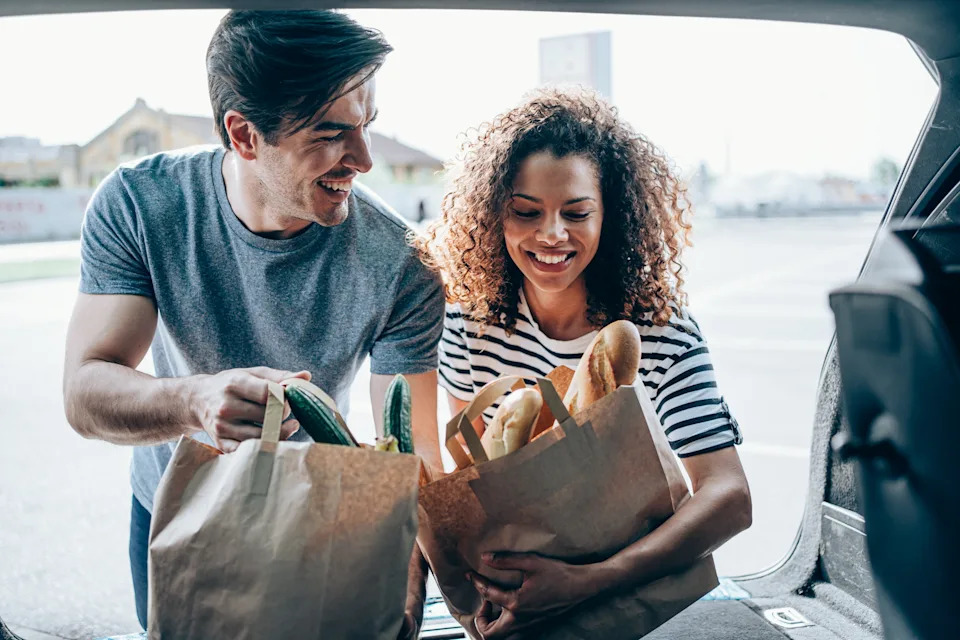 Couple placing groceries into a car trunk, smiling