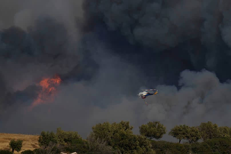 Un hélicoptère vole à travers la fumée d'un incendie à Keratea, dans la banlieue d'Athènes, le vendredi 8 août 2025.