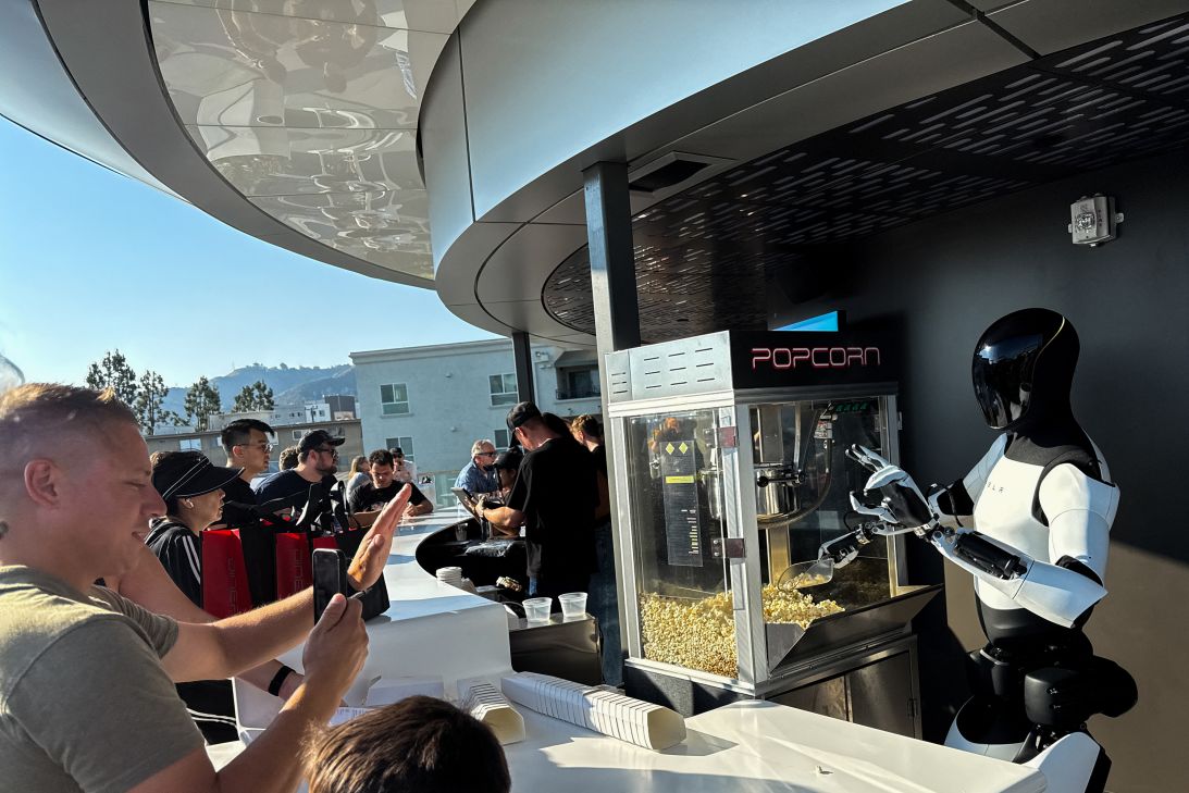 A Tesla Optimus robot scoops popcorn and gestures at attendees during the opening of the Tesla Diner on July 21, 2025.