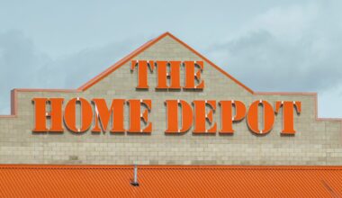The Home Depot store exterior with large orange letters spelling "The Home Depot" on a beige brick wall and an orange roof below, set against a cloudy sky.