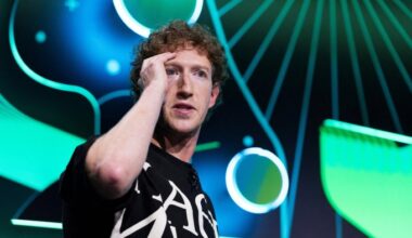 Mark Zuckerberg gestures near his face during a live technology podcast recording, with abstract green and blue graphics in the background