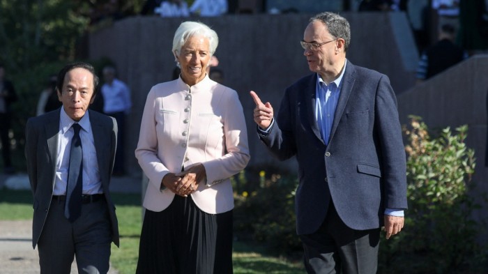 Christine Lagarde, Kazuo Ueda, and Andrew Bailey walk together outdoors, with Bailey gesturing as they converse.
