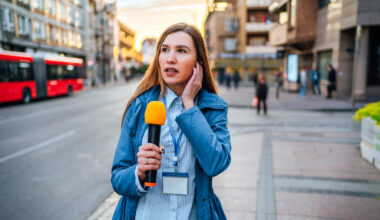 Young female reporter with microphone on city street during live broadcast