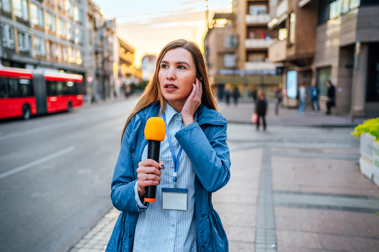Young female reporter with microphone on city street during live broadcast