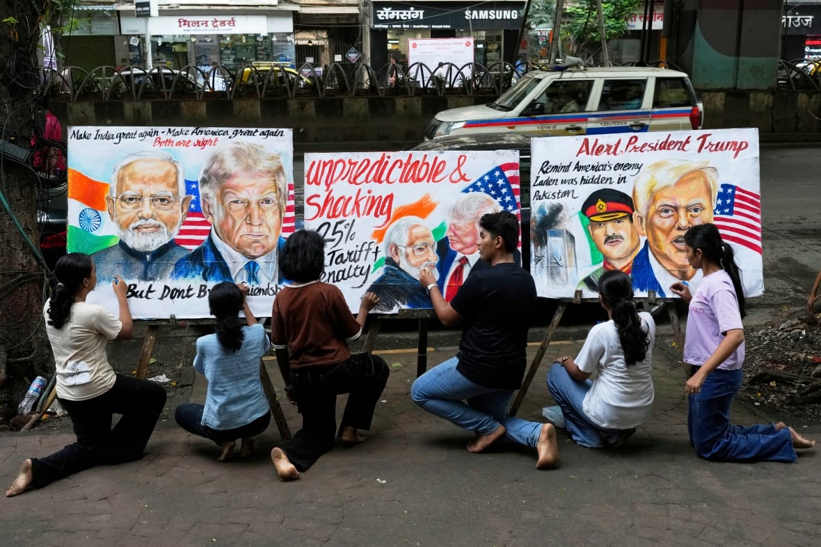 People kneel in the streets and paint three protest banners featuring U.S. President Donald Trump and Prime Minister of India Narendra Modi and protest slogans against tariffs.